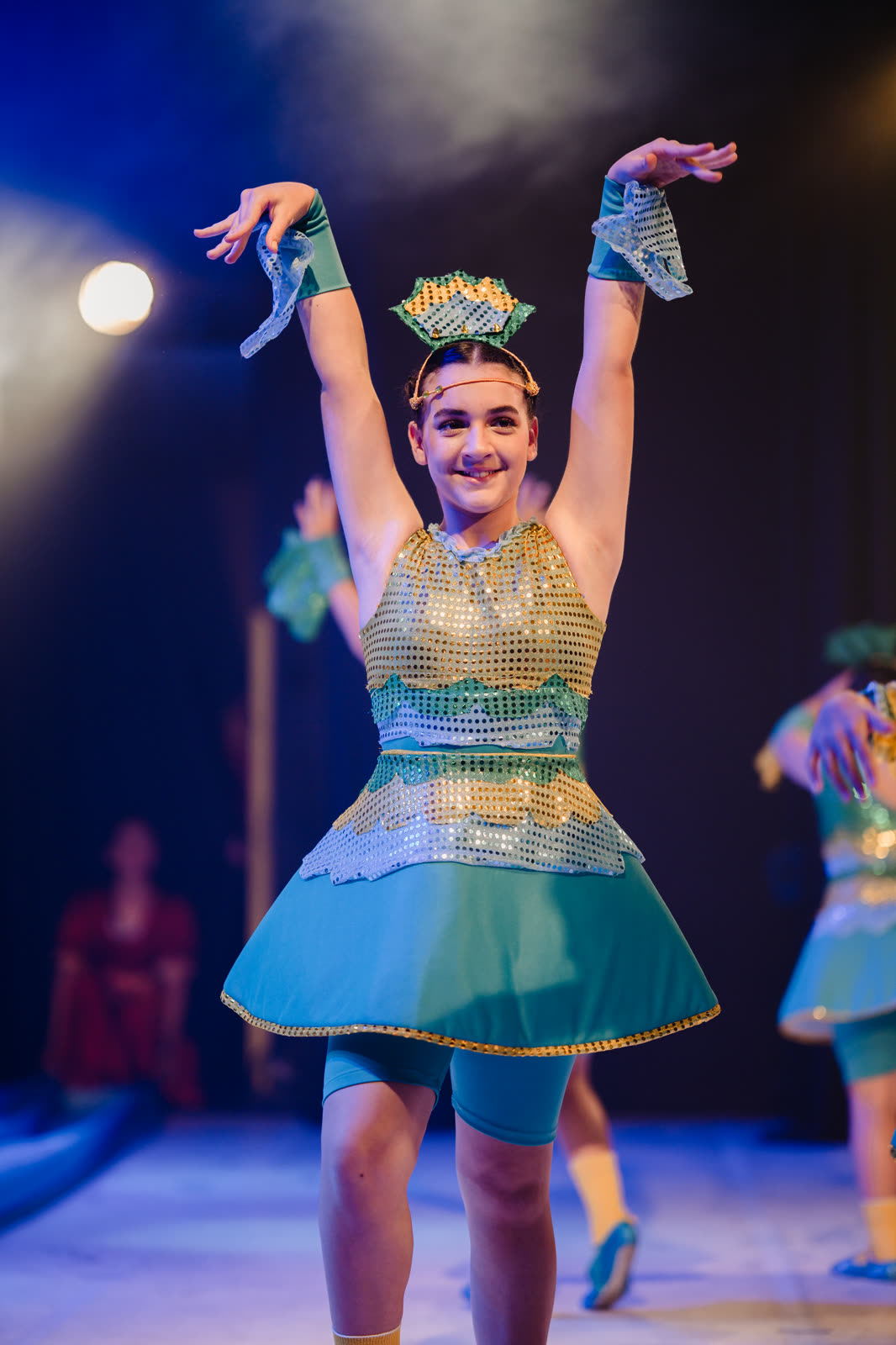 Bailarina de verde e dourado com os braços erguidos no palco